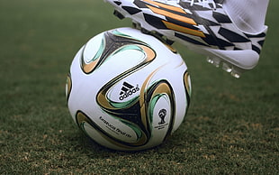 white, brown, teal, and black Adidas soccer ball on green grass field