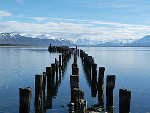 brown wooden dock stand on body of water near mountain during daytime