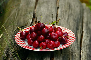 plate of red Cherries on brown wooden surface closeup photography