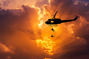 photo of helicopter silhouette with two person gliding down during golden hour