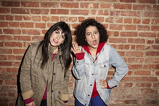 two women wearing jacket standing beside a concrete brick wall