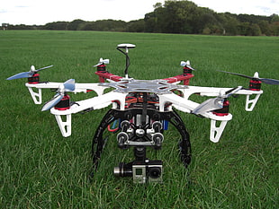 white, red, and black drone with action camera on green grass