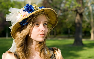 girl in brown sun hat with trees and grass field in the background