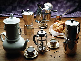 stainless steel moka pot, coffee press, grey ceramic teapot, and teacup and saucers