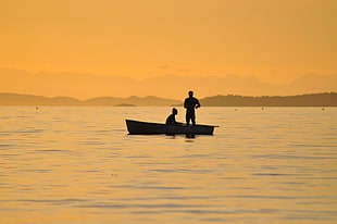 silhouette photo of two person on boat in middle of body of water during golden hour \