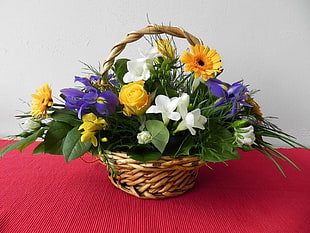 basket of purple Irises, yellow Gerberas, and white Lilies on red table