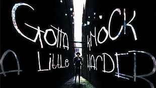 man in black standing between two wall with Gotta Little Knock Harder sign