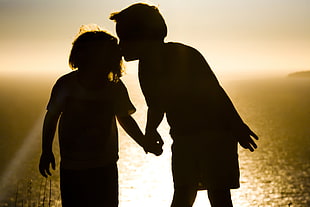 boy kissing girl while holding hands facing body of water