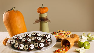 cupcakes serve on plate near pumpkin and chalice on table