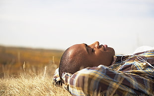 closeup photo of a man wearing brown, yellow, and blue plaid pattern sport shirt lying on ground