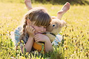 photography of girl lying on grass while doing right arm rest and holding teddy bear