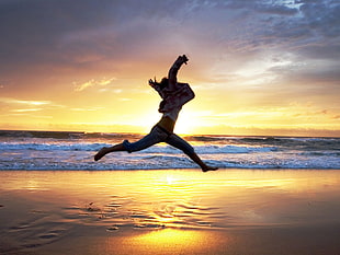 woman jumping near beach shore during golden hour HD wallpaper