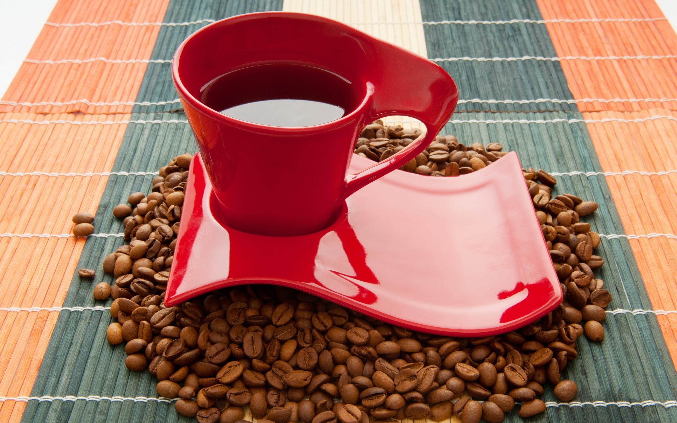 red coffee mug on saucer surrounded with coffee beans