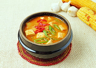 yellow soup with tofu,green and red peppers on black ceramic pot