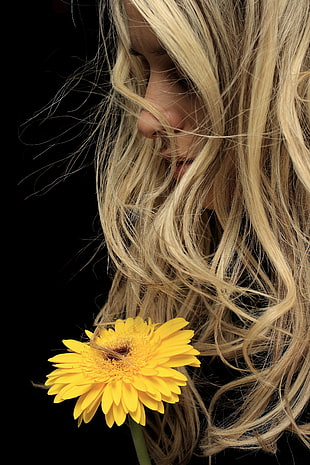 woman with blonde wavy hair in front of sunflower with black background