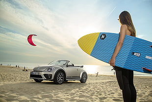 woman holding surfboard near gray Volkswagen Beetle