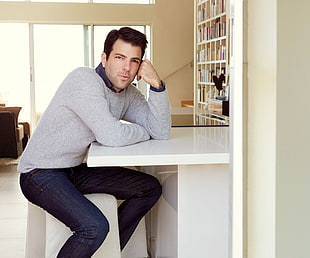 man in gray sweater sitting near white wooden table inside room