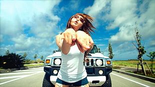 woman pointing fingers in front of Hummer on road at daytime