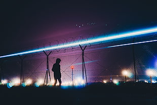 silhouette photo of boy walking near gray chain-link fence