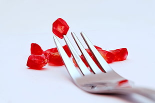 close-up photo of red jelly food with stainless steel fork, pomegranate