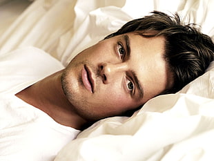 man in v-neck shirt laying on white bedspread