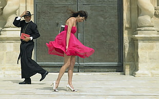 woman wearing pink straight-across dress near man wearing black robe during daytime