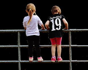 photograph of two girls on gray metal fence
