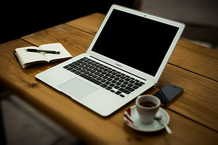 MacBook Air between notebook, black iPhone and ceramic teacup on saucer on top of wooden table HD wallpaper