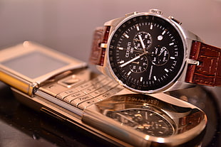silver-colored chronograph watch on gray candybar phone
