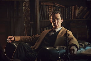 man wearing brown coat sitting on black leather armchair inside room