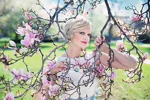 woman in white sleeveless top holding tree branch with pink petaled flowers
