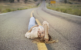 woman wearing white long-sleeve shirt laying down on highway during daytime