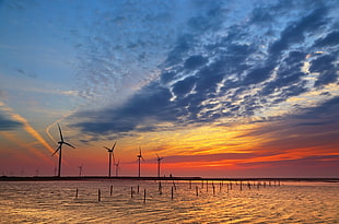 four black wind mills during sunset