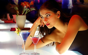 woman leaning on glass table beside two cocktail drink on martini glasses