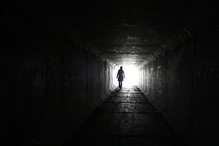 person walking inside dark tunnel with white light on far distanc