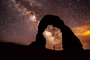 silhouette of a person under stone arch under starry sky HD wallpaper