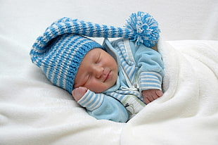 baby in blue shirt and cap sleeping on white textile