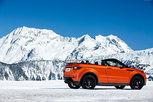 photography of orange convertible coupe next to snow capped mountain during daytime