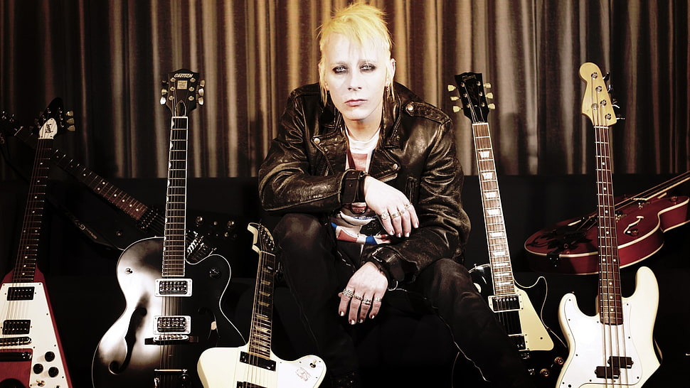 man in black leather jacket sitting beside guitars HD wallpaper