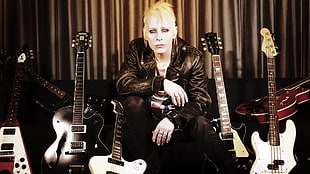 man in black leather jacket sitting beside guitars