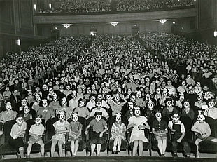 crowd of people covering face with mask sitting down in theater chairs