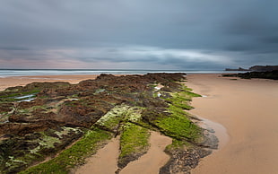 rock formation near sand and body of water under dark skies