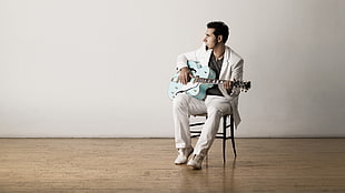 man in white suit playing guitar inside white painted room