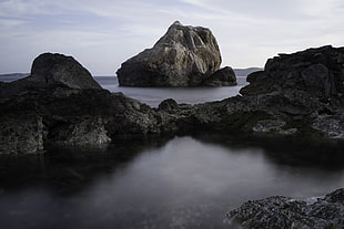 landscape photography of rock formation surrounded by water under cloudy sky