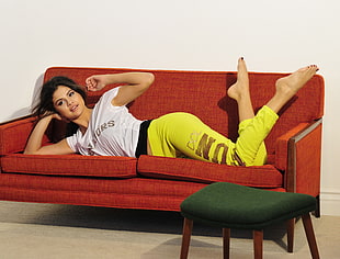 woman wearing white cap-sleeve shirt and yellow sweatpants lying on red 2-seat sofa
