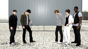 five men stands in front of a gray metallic wall