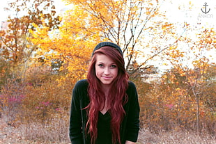 woman wearing green v-neck shirt and black knit cap standing near trees during daytime