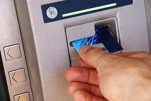 person holding blue ATM card inserting on ATM machine