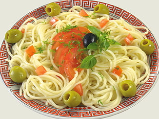 pasta dish with sliced tomatoes and olives served on red and white ceramic bowl