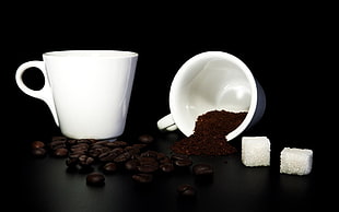 two white ceramic mugs with coffee beans and sugar cubes